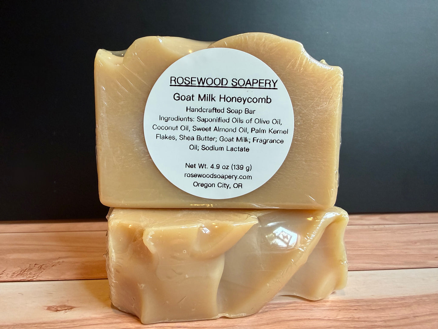 Two goat milk honeycomb soap bars with a label on a wooden surface and dark background