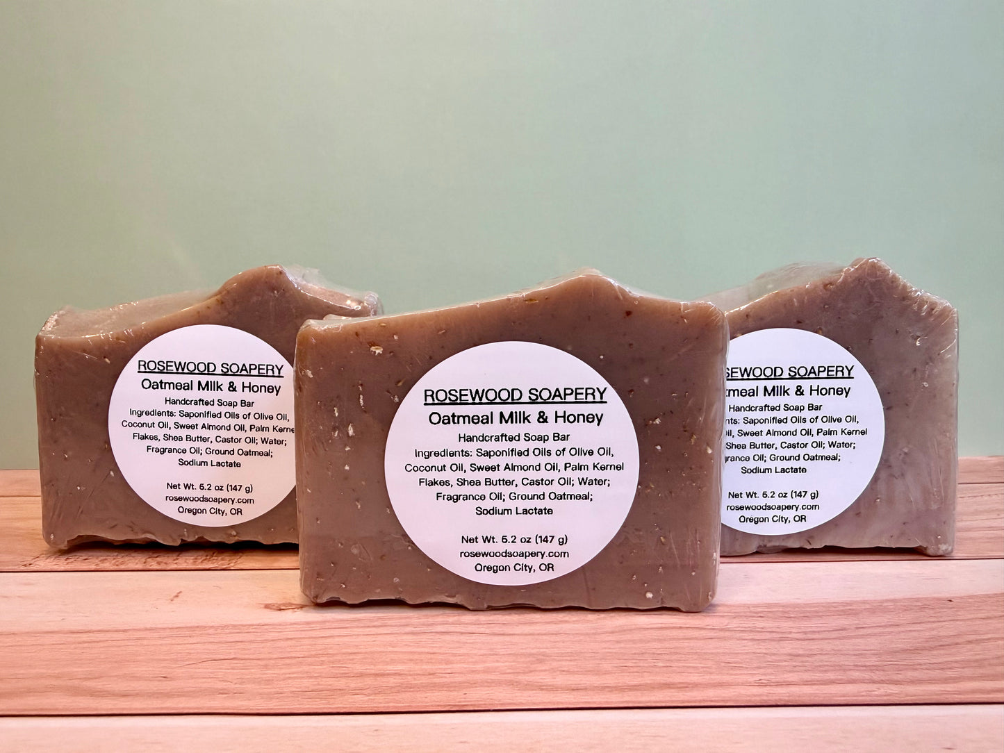 3 bars of oatmeal soap with labels, sitting on a wooden surface.