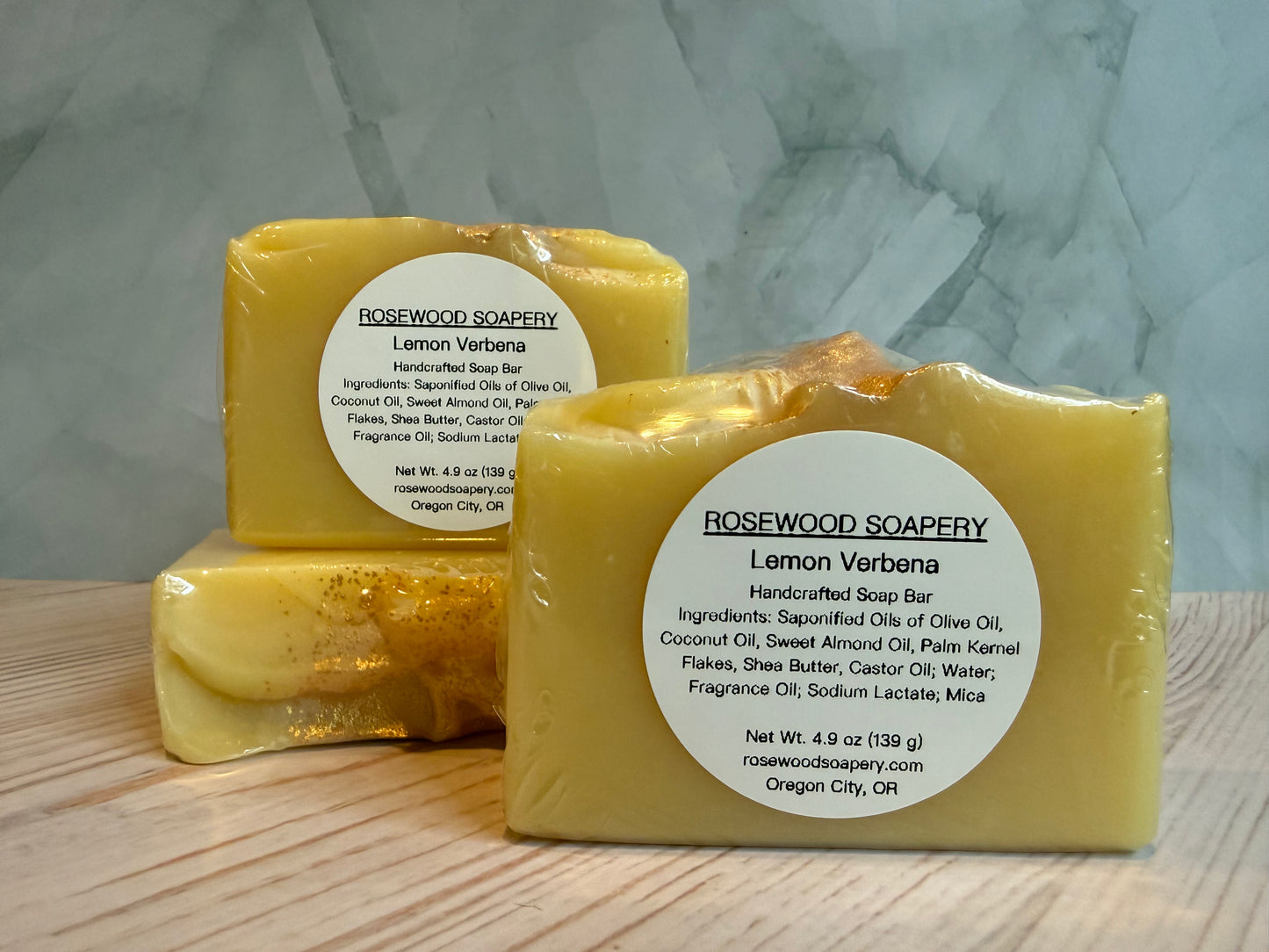 Two bars of Lemon Verbena soap from Rosewood Soapery on a wooden surface with a gray marble background.