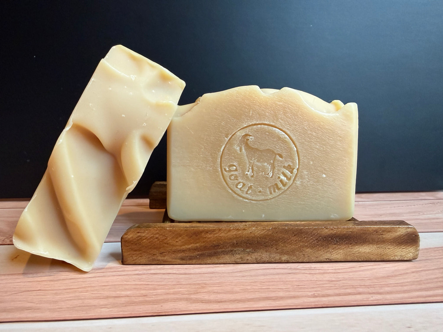 Two cream colored soaps against a black background on a wooden surface. 
