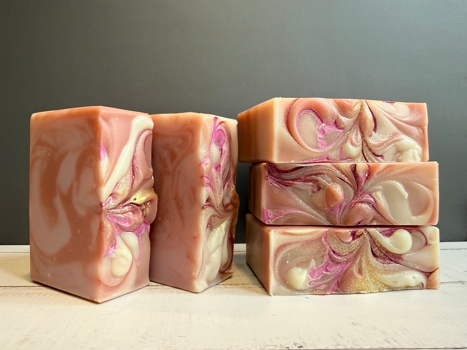 Five pink soaps against a gray background on a wooden surface. 