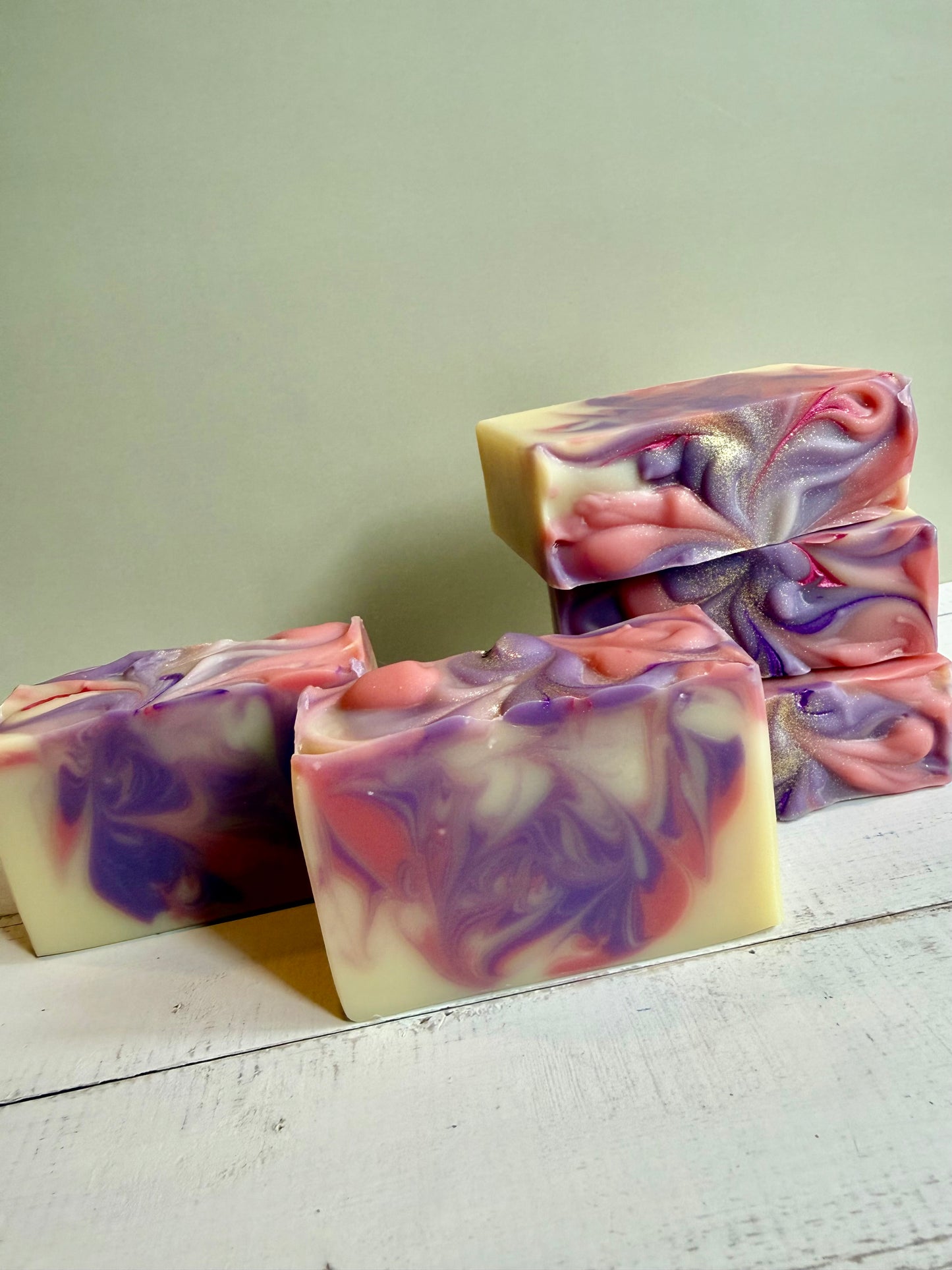 Handmade soap bars with purple and pink swirls on a wooden surface.
