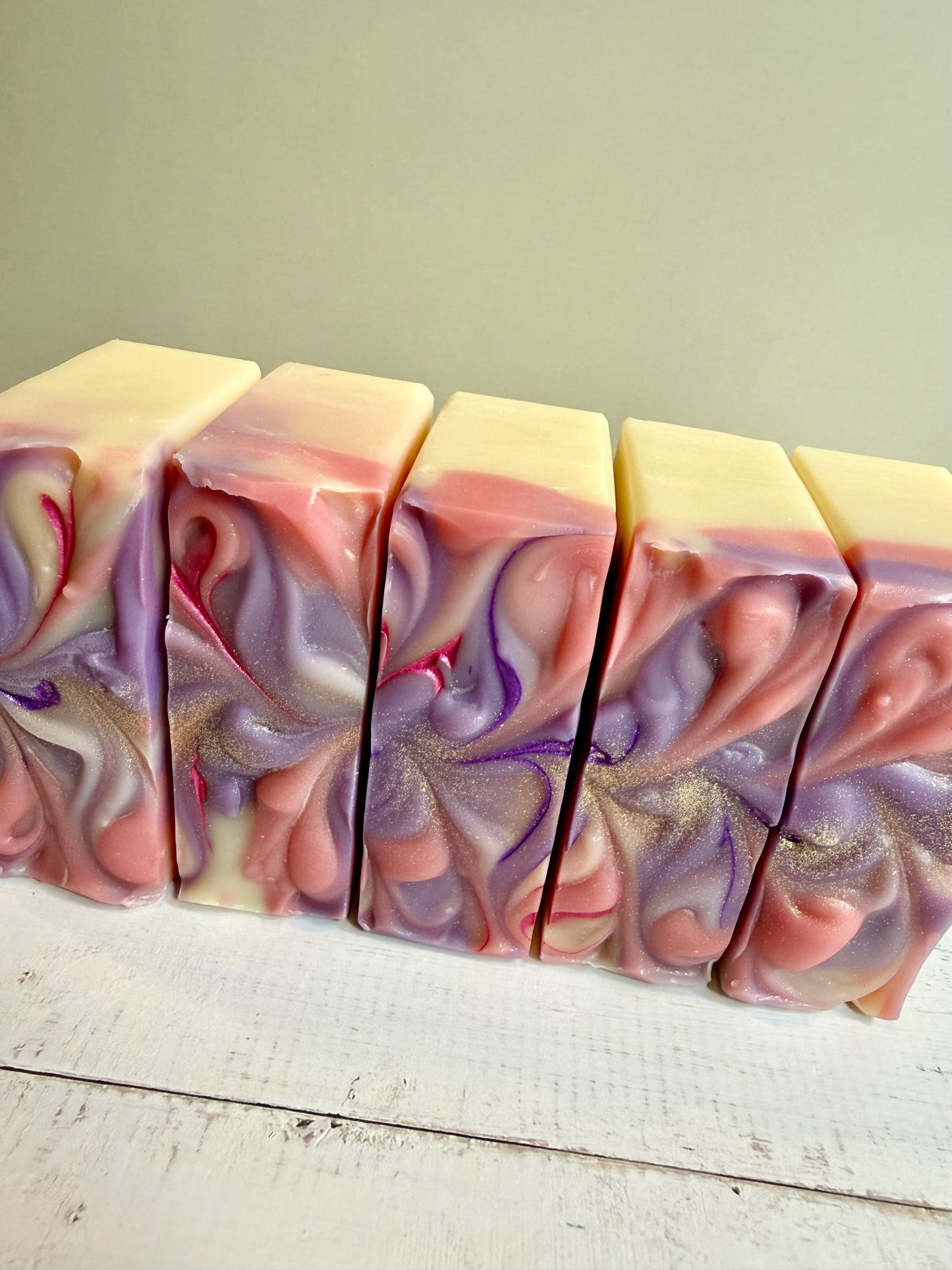 Five bars of swirled soap with pink and purple hues on a light wooden surface.