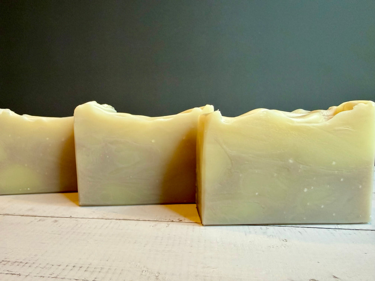 Three handmade rectangular bars of soap with wavy tops, made from a pale creamy yellow marbled soap blend, standing on a white wooden surface against a dark gray background.