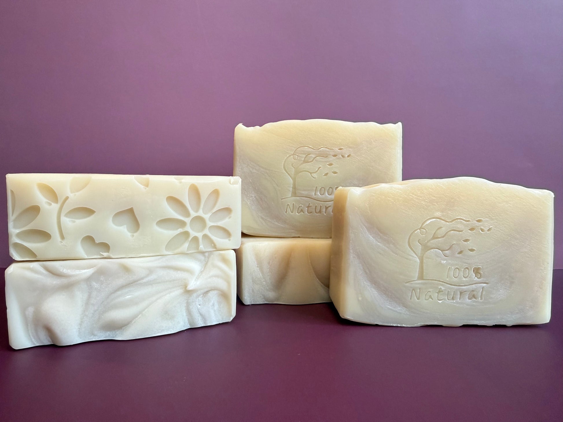 Five bars of natural soap with embossed designs on a purple background