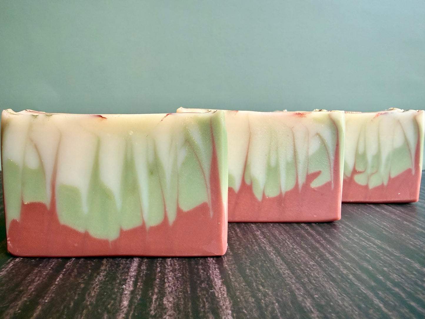 Three bars of soap with a brown and green gradient on a wooden surface.