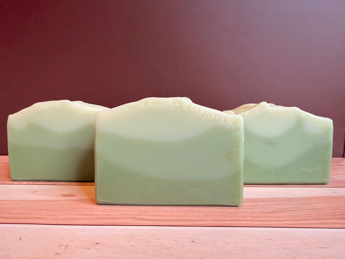 Three bars of green soap on a wooden surface with a dark background