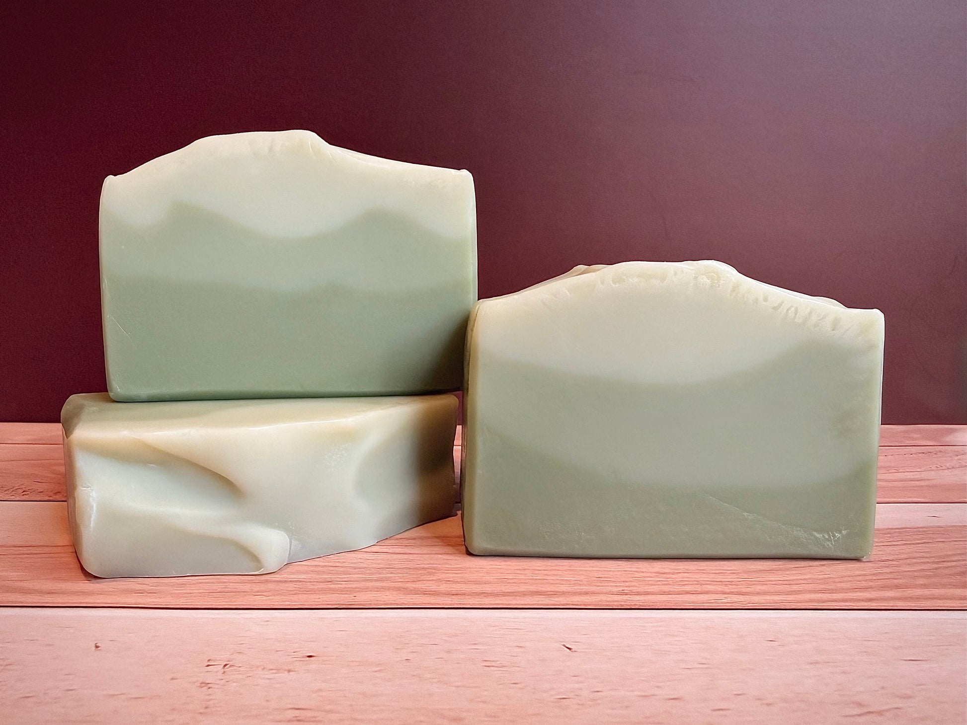 Three bars of green soap on a wooden surface with a brown background