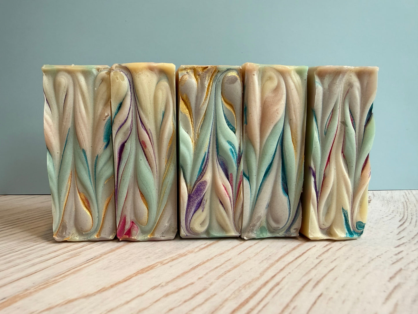 Five bars of handcrafted soap with colorful swirl patterns on a wooden surface.