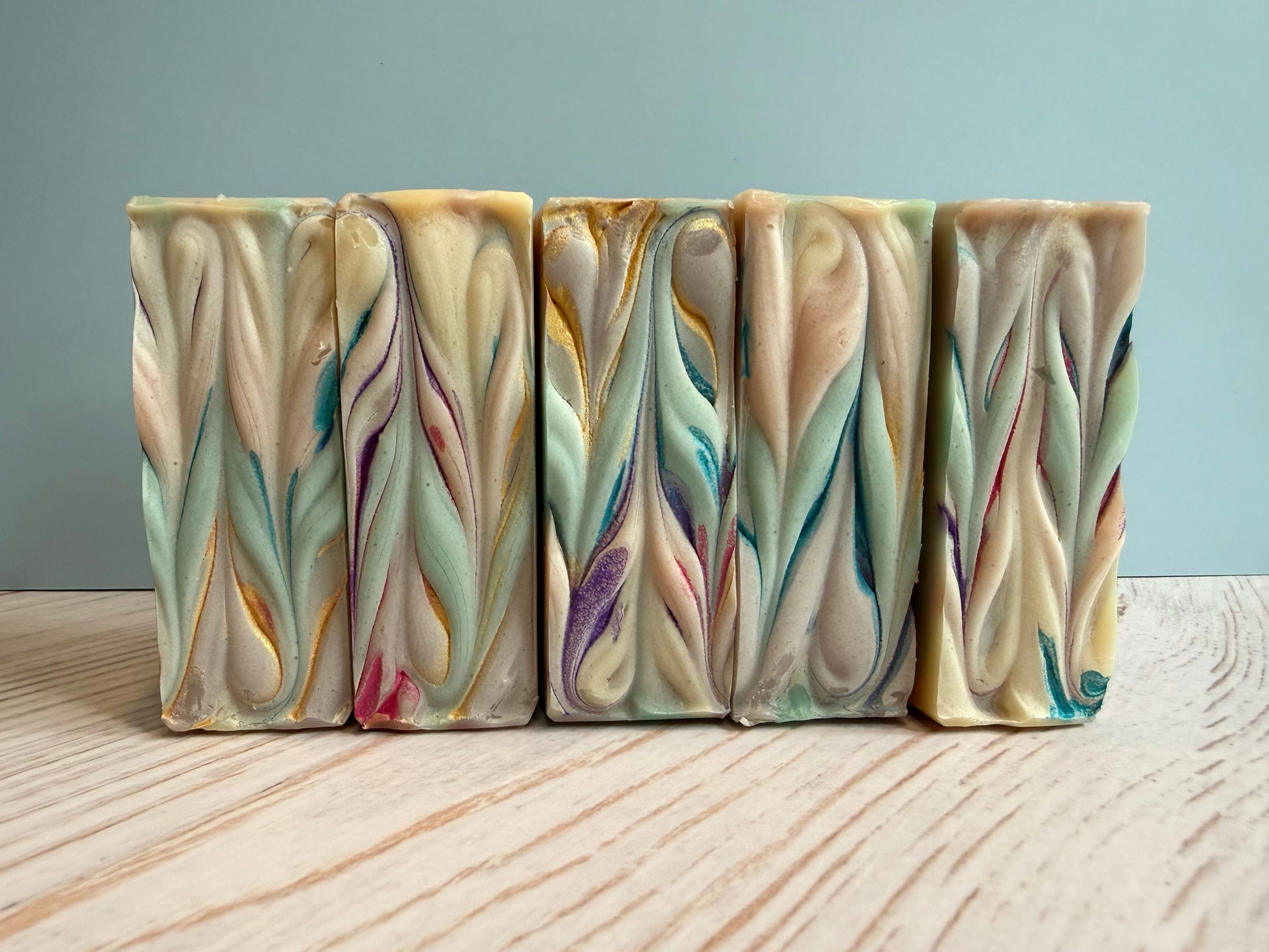Five bars of handcrafted soap with colorful swirl patterns on a wooden surface.