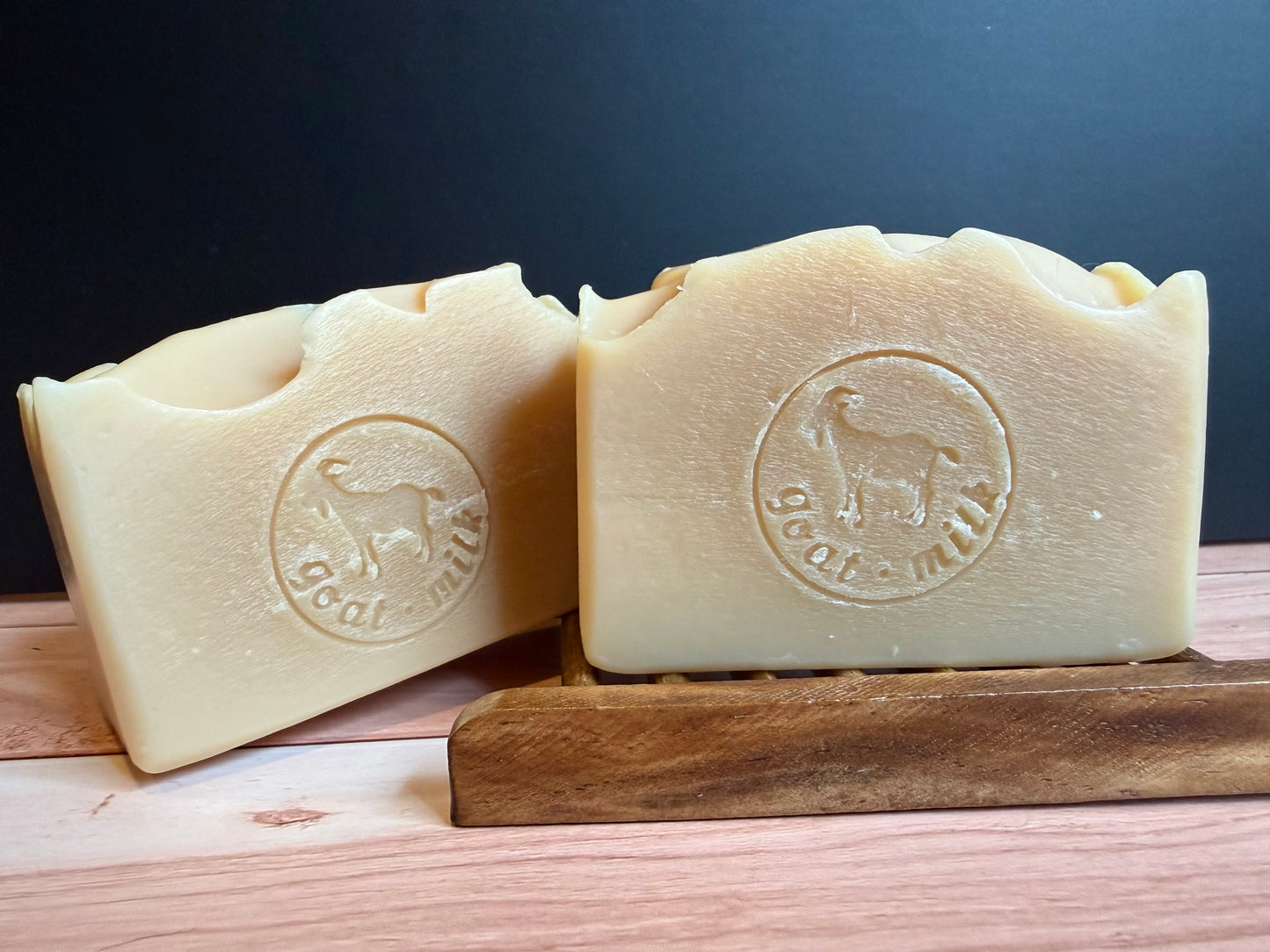 Two bars of goat milk soap on a wooden stand with a dark background