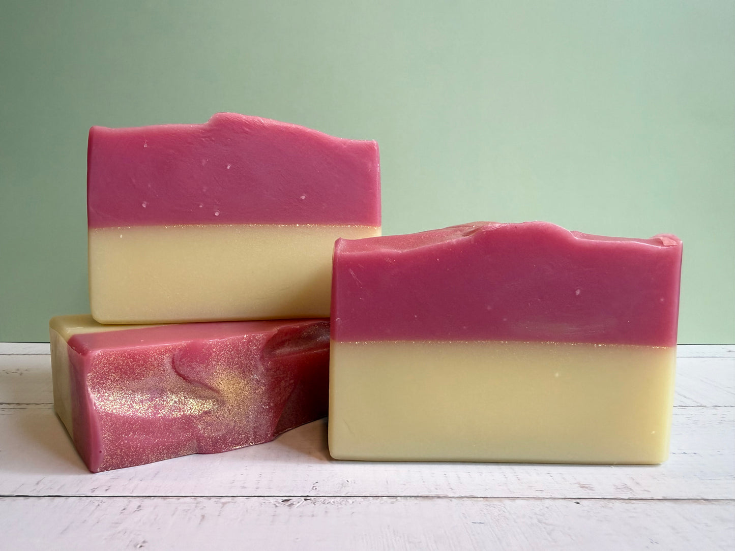 Three layered soap bars with pink and yellow colors on a wooden surface.
