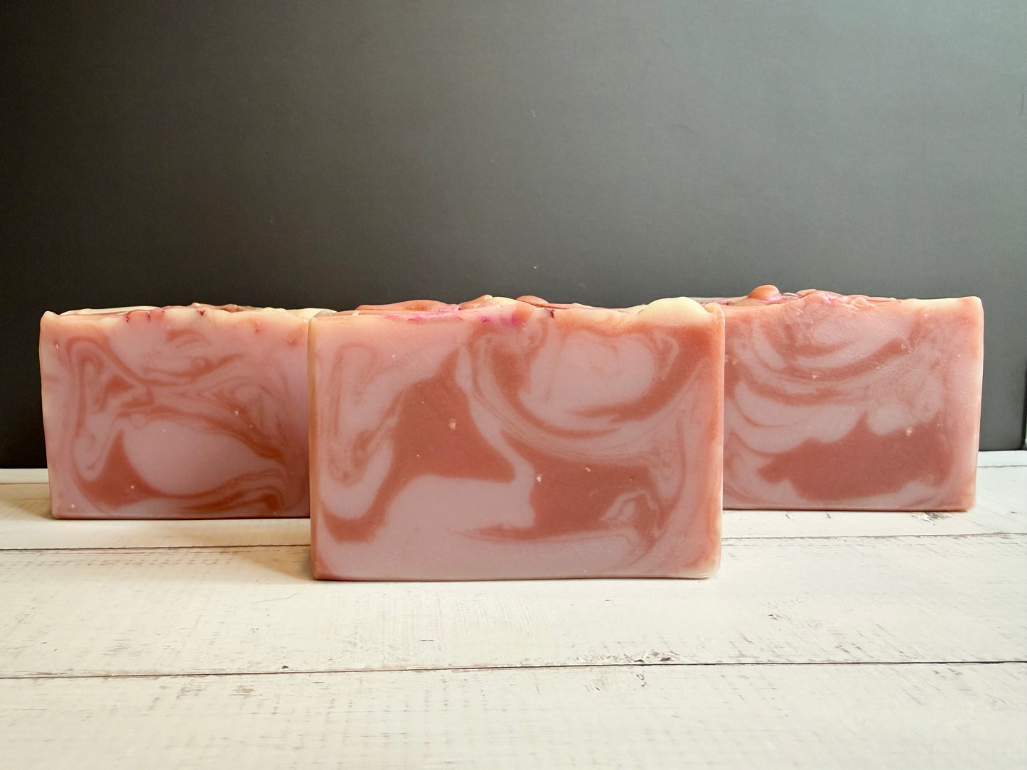 Three bars of marbled pink and white soap on a wooden surface with a gray background