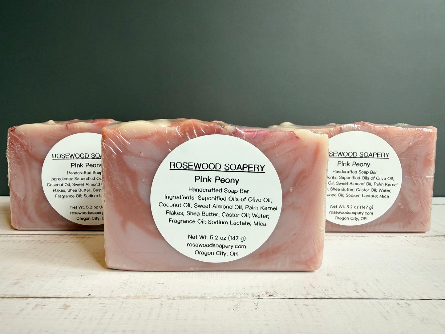 Three bars of Rosewood Soapery Pink Peony soap on a wooden surface with a gray background
