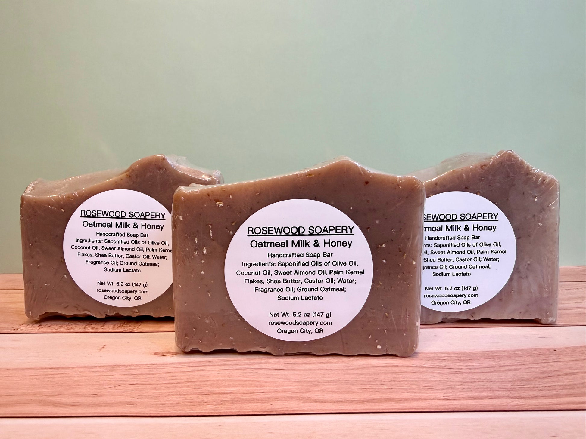 3 bars of oatmeal soap with labels, sitting on a wooden surface. 