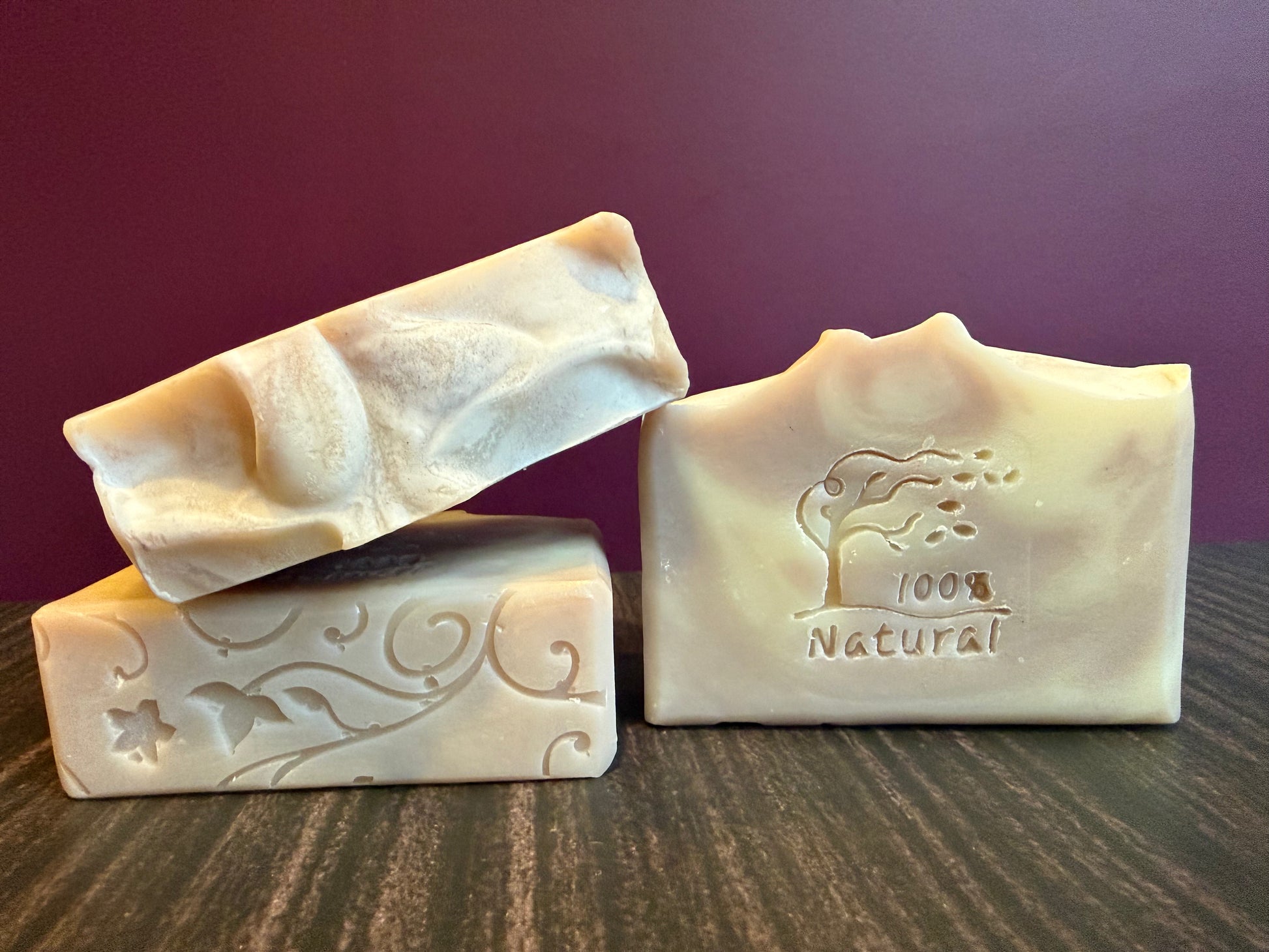 Three bars of soap with embossed designs on a wooden surface against a dark purple background