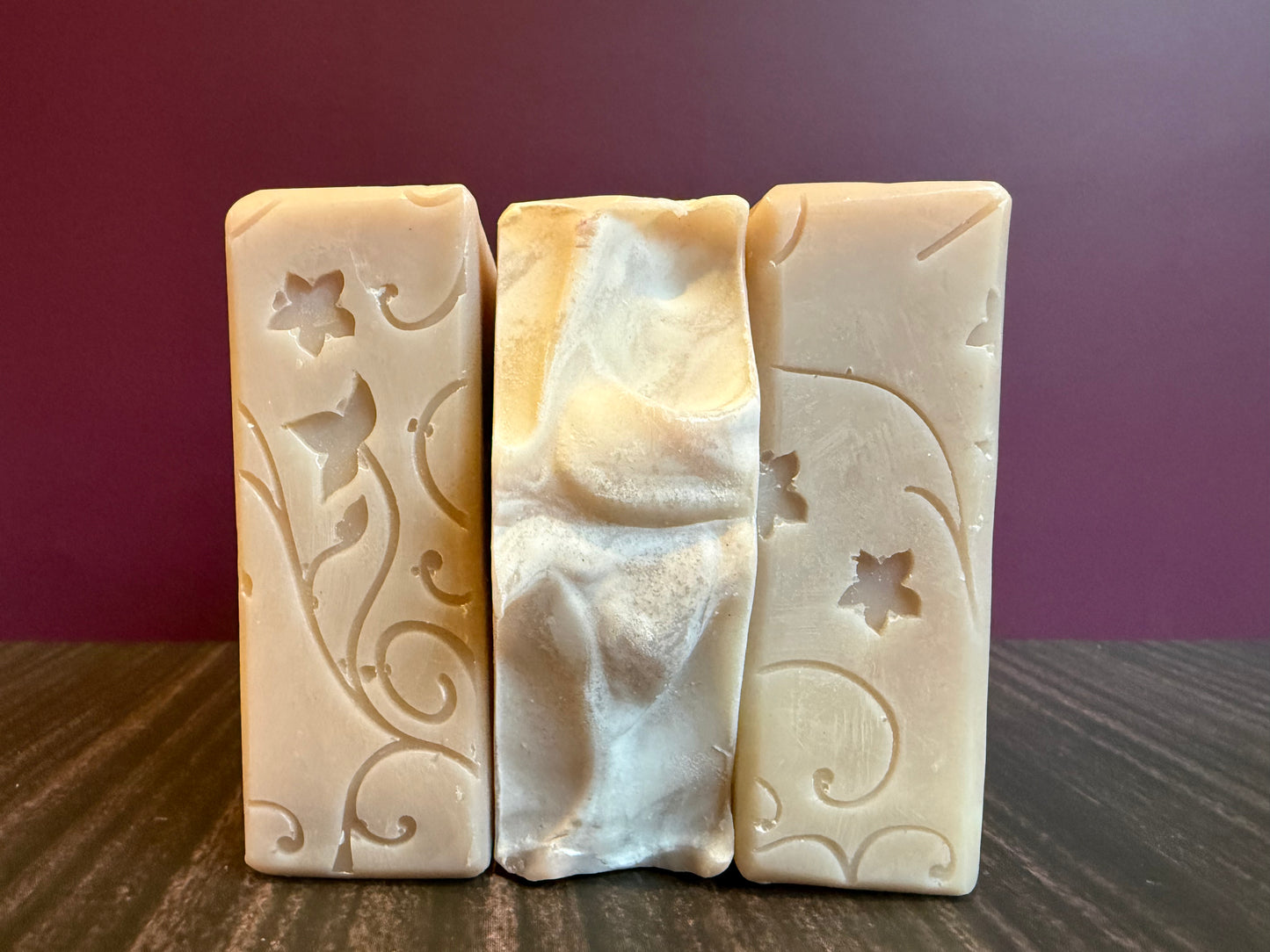 Three bars of soap with decorative patterns on a wooden surface and purple background