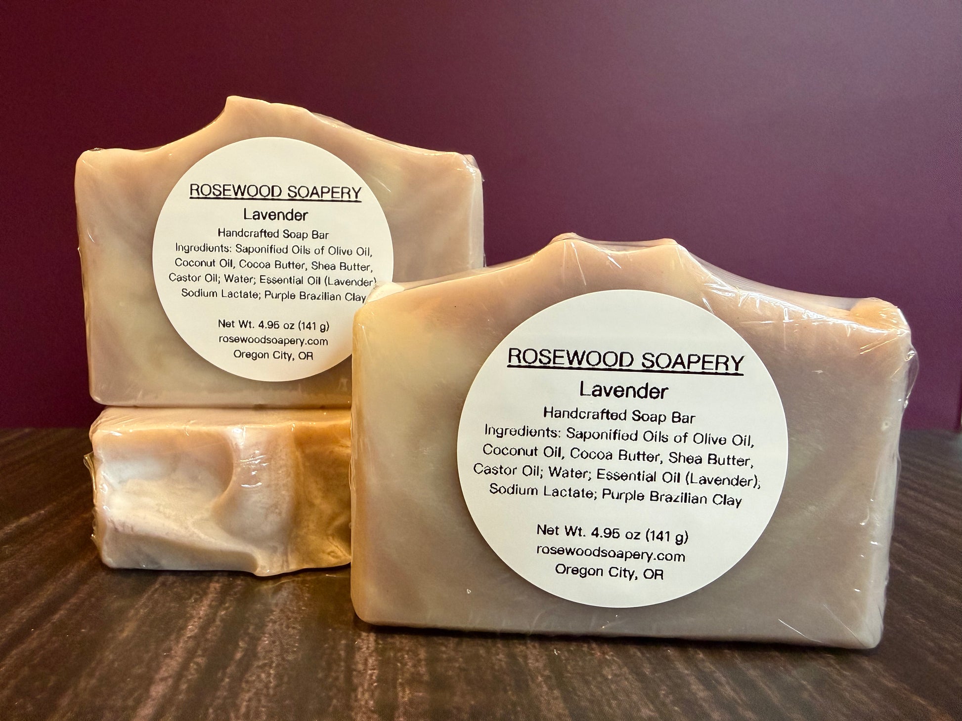 Two bars of lavender soap from Rosewood Soapery on a wooden surface with a purple background.