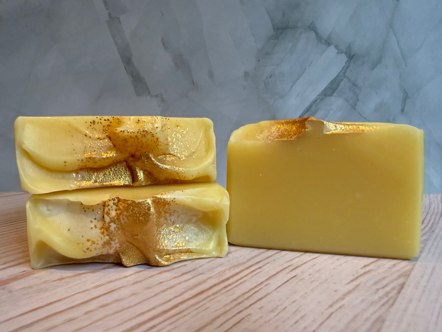 Two yellow soap bars on a wooden surface with a marble background