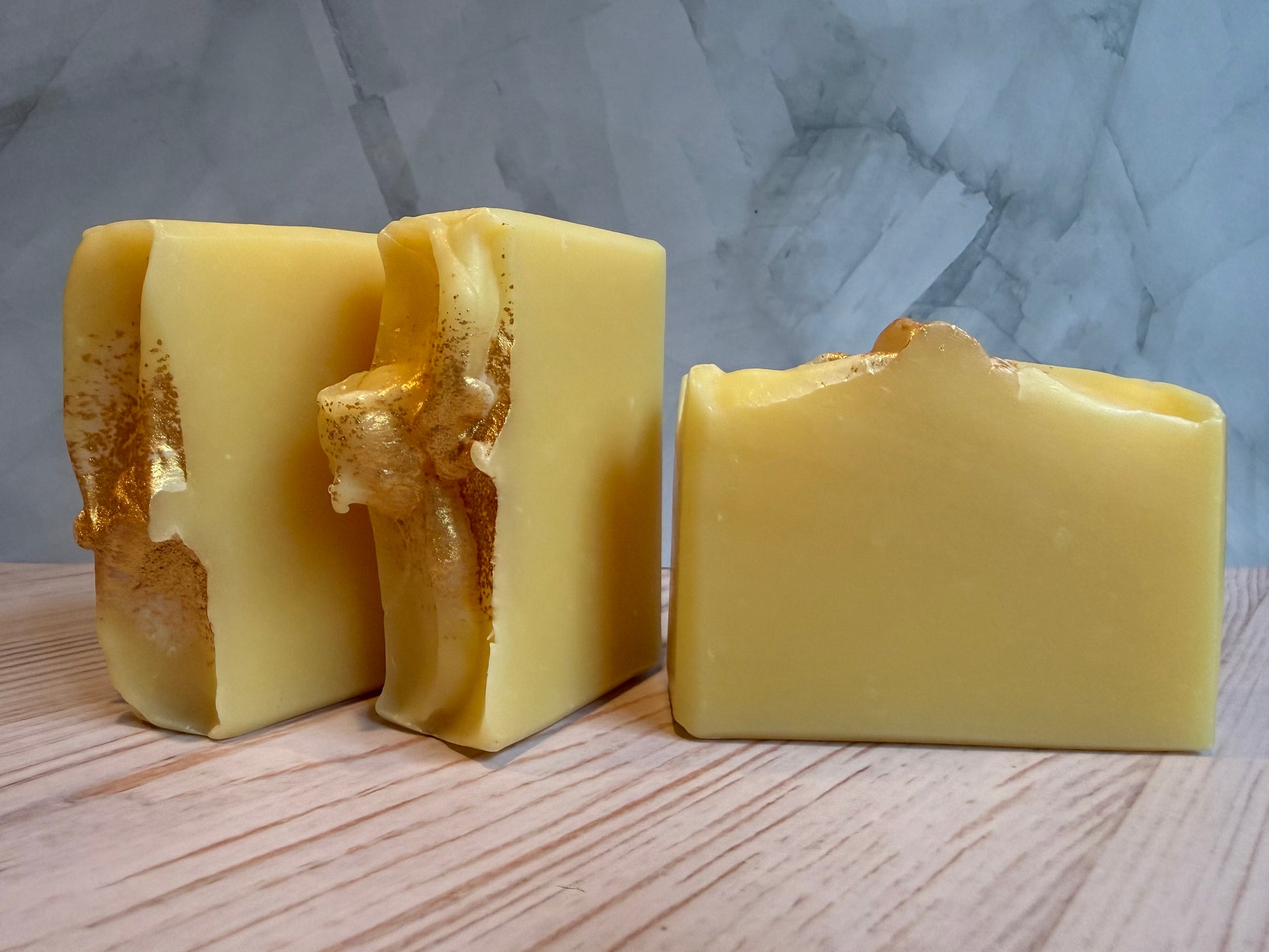 Three pieces of yellow soap on a wooden surface with a marble-patterned wall in the background.